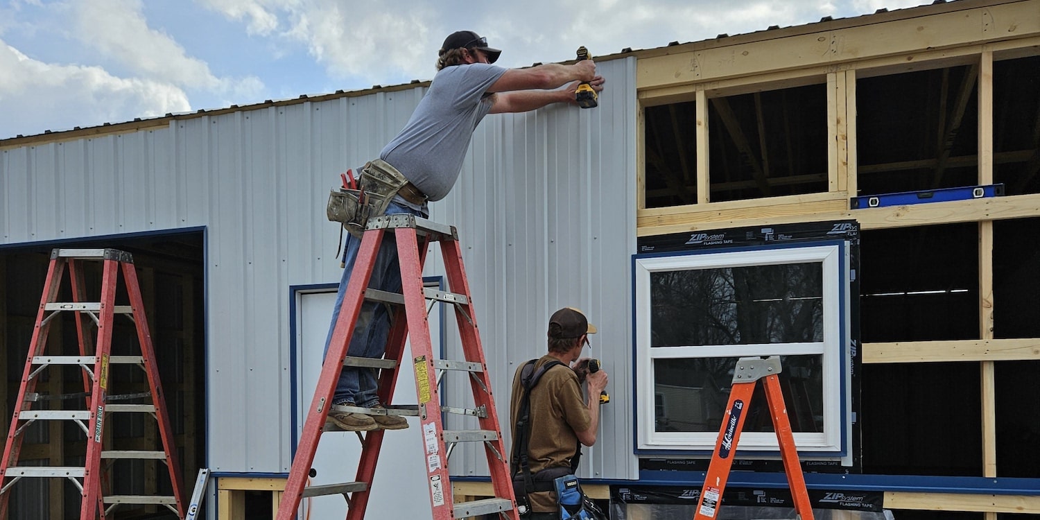 Two employees drilling white siding on a commercial project