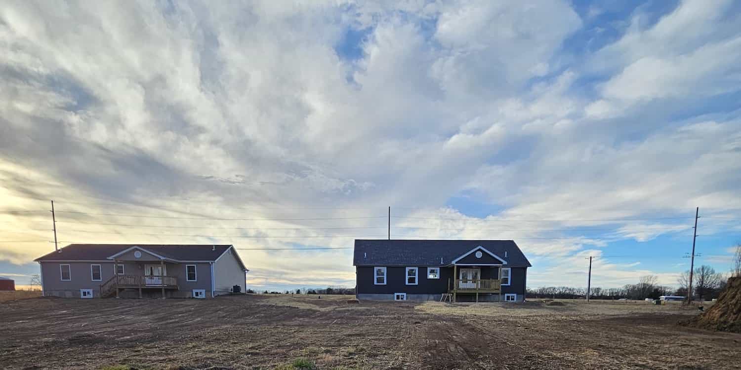 Two residential houses (one tan and one blue) with a beautiful cloudy, sunny backdrop