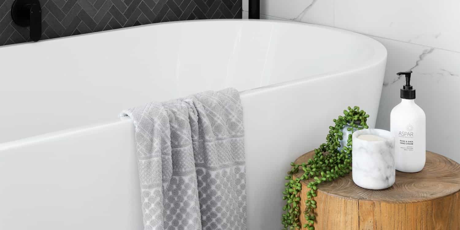 A white tub in a bathroom, with soap, a candle sitting on a wood table